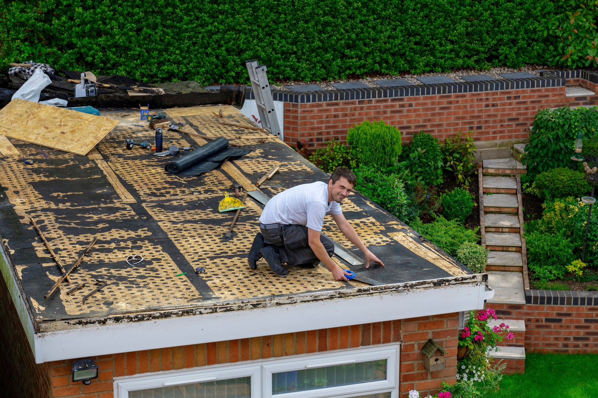 A carpenter using a handsaw on a flat garage roof as he prepares it for a fibre glass coating.